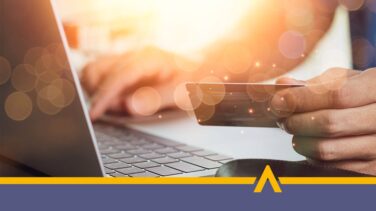 Osoba trzymająca kartę płatniczą przy laptopie podczas płatności online