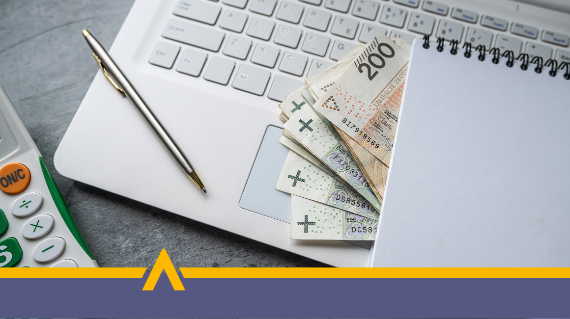 Polskie banknoty wystające spod zeszytu na klawiaturze laptopa